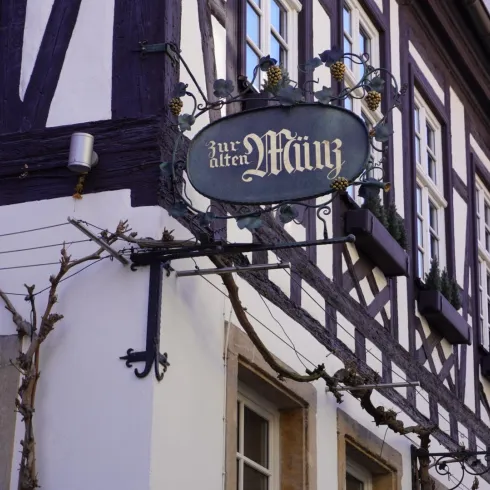 Ein historisches Fachwerkgebäude mit einem dekorativen Schild. Das Schild trägt den Namen "zur alten Männz".
