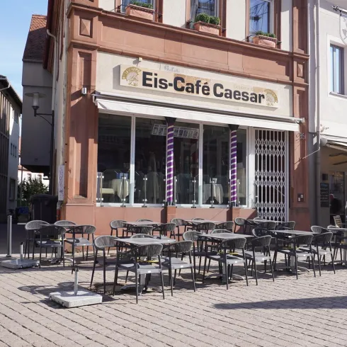 Ein gemütliches Eiscafé mit Tischen und Stühlen im Freien. Die Fassade ist freundlich und einladend gestaltet.