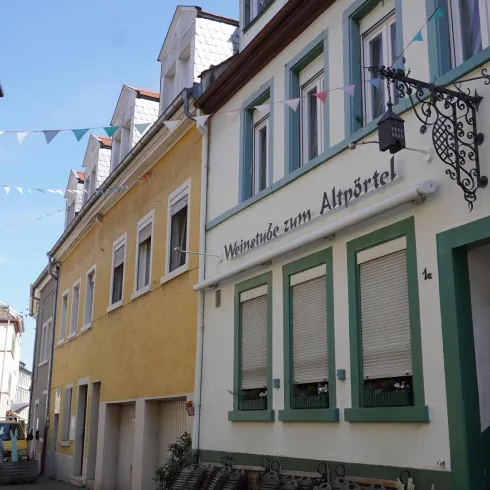 Eine malerische Gasse mit bunten Häusern und Wimpeln. Im Vordergrund steht ein Gasthaus mit einem einladenden Schild.
