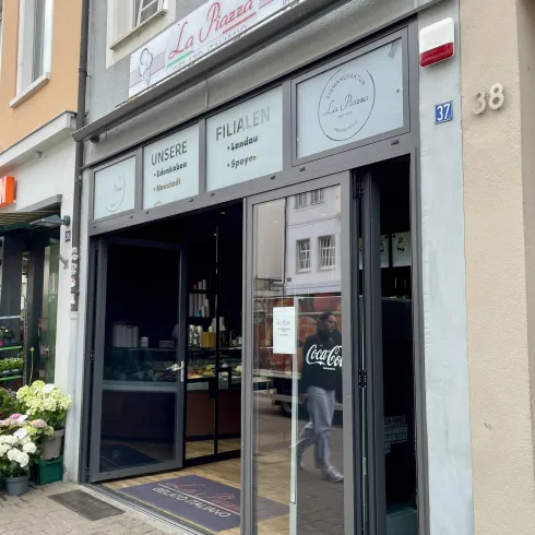 Ein kleines Café namens "La Panna" mit großen Glasfronten. Draußen stehen Blumen und der Eingang ist einladend gestaltet.