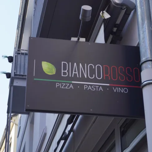 Ein Schild mit dem Namen "Bianco Rosso" in der italienischen Küche. Es wird Pizza, Pasta und Wein angeboten.