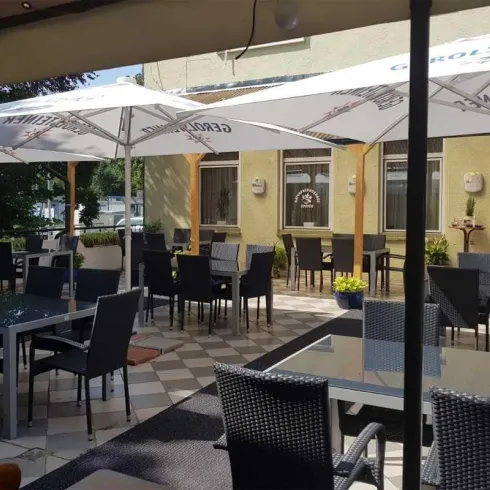 Eine gemütliche Terrasse mit Tischen und Stühlen, überdacht von Schirmen. Ein gastlicher Ort, ideal zum Entspannen und Genießen.