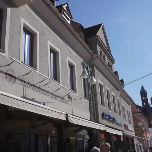 Eine belebte Straße mit modernen Gebäuden und Geschäften. Im Hintergrund sind historische Türme zu sehen.