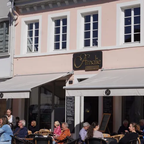 Ein gemütliches Café mit Außensitzplätzen und Sonnenschirmen. Viele Menschen genießen ihre Zeit bei Kaffee und Gesprächen.