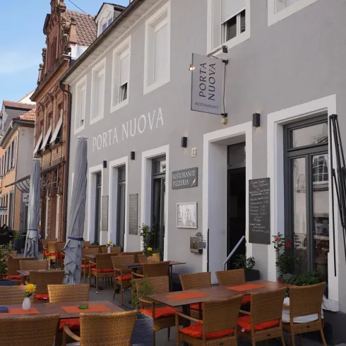 Ein Restaurant mit gemütlichen Terrassenstühlen und Tischen im Freien. Die Fassade des Gebäudes ist modern und einladend.