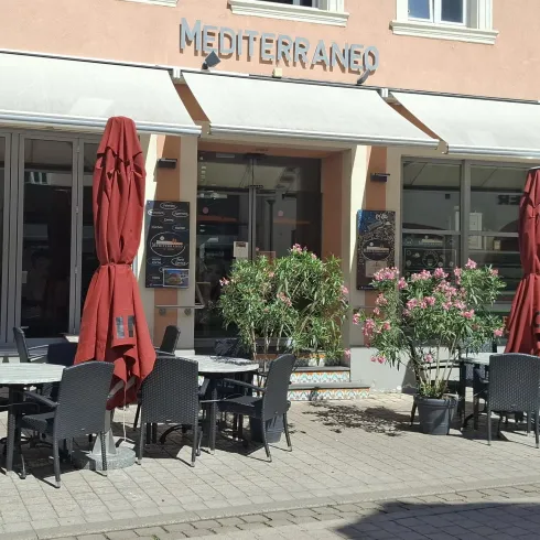 Ein mediterranes Restaurant mit Außenbereich. Rote Sonnenschirme und Tische laden zum Verweilen ein.