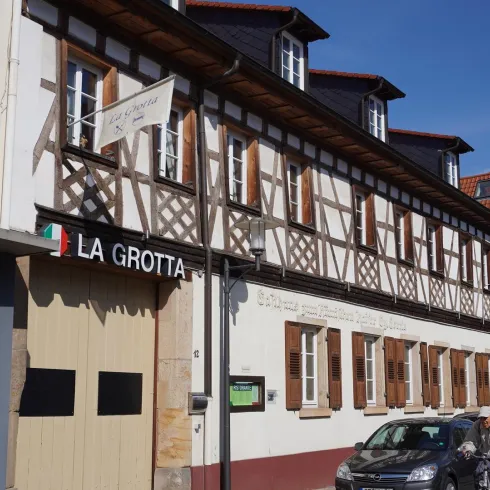 Ein historisches Gebäude mit Fachwerk und einem Schild, das "LA GROTTA" anzeigt. Die Fassade hat viele Fenster und befindet sich in einer Stadtstraße.