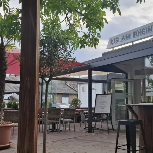 Ein einladendes Restaurant im Freien mit Palmen und Tischen. Der Himmel ist bewölkt, und die Atmosphäre ist gemütlich.