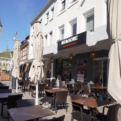 Ein Restaurant mit Tischen im Freien und Sonnenschirmen. Im Hintergrund ist ein historischer Turm zu sehen.