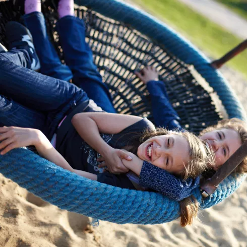 Zwei Personen in einer Korbschaukel auf einem Spielplatz