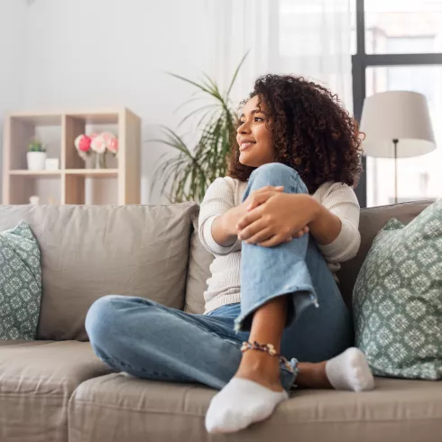 Eine Frau sitzt mit einem angewinkelten Bein auf einem Sofa