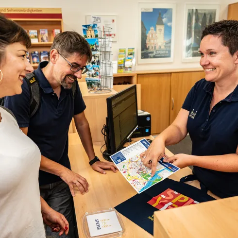 Drei Personen stehen an einem Empfangscounter und lächeln sich an