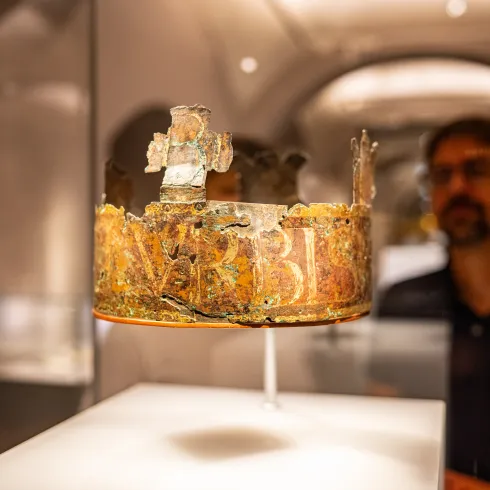 Mittelalterliche Krone in einer Glasvitrine, im Hintergrund steht ein Mann