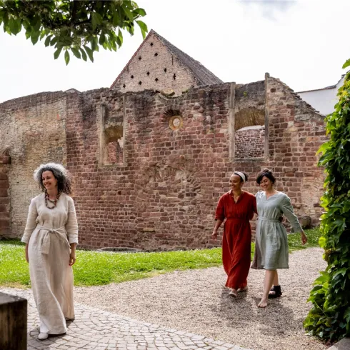 Drei gewandete Frauen laufen über das Areal des Judenhof in Speyer