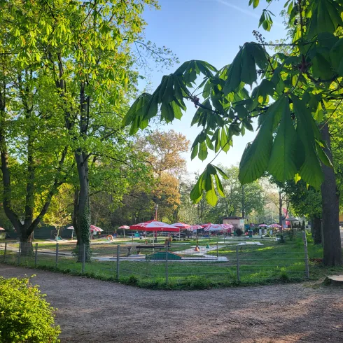 Grüne Bäume und Büsche, ein Weg aus feinen Kieselsteinen und im Fokus eine Minigolfanlage